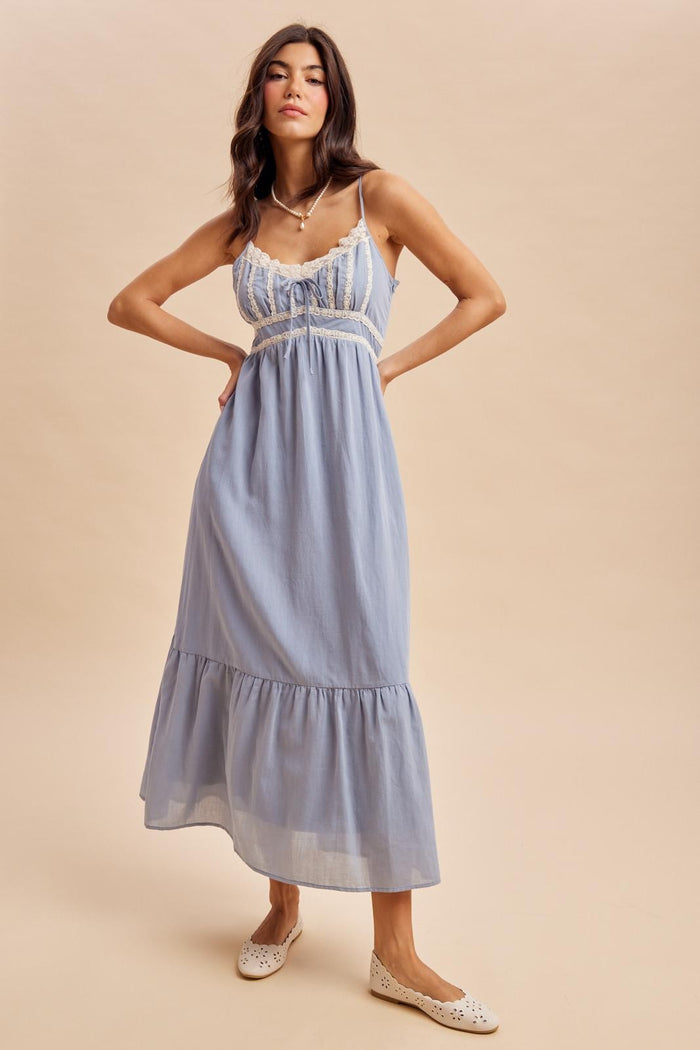 woman wearing a light blue maxi dress with lace details and a tiered skirt, styled with white flats