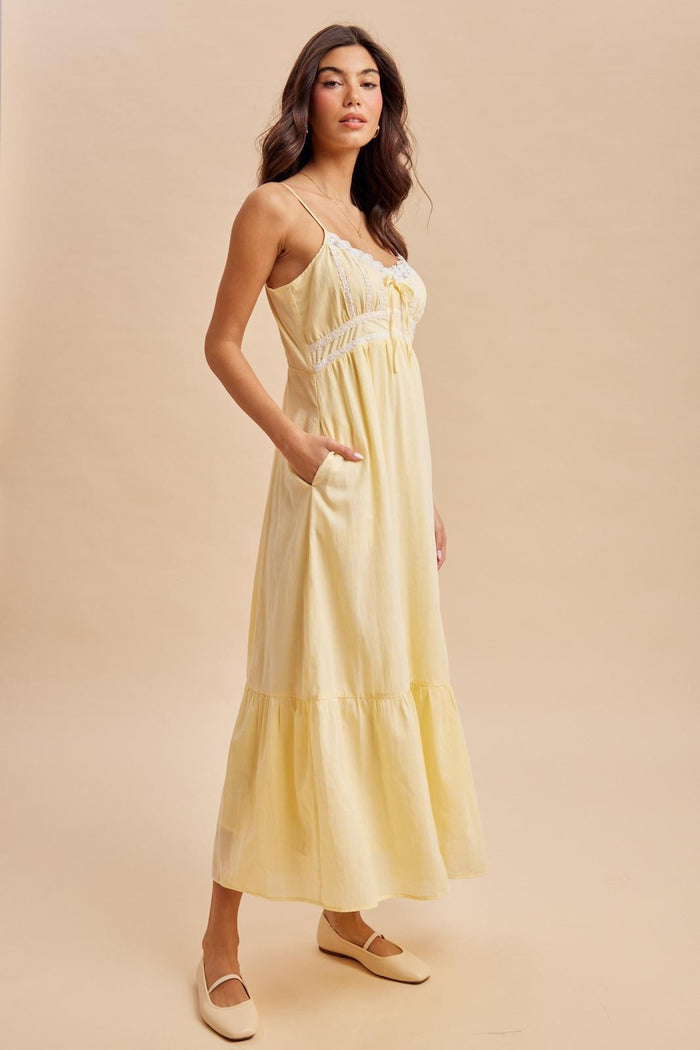 woman wearing a yellow maxi dress with a tiered hem and pockets, styled with neutral flat shoes