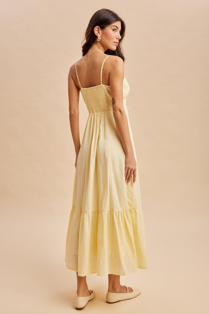 woman wearing a yellow maxi dress with a smocked bodice and tiered skirt, styled with simple slip-on shoes