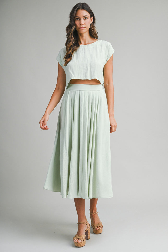 woman wearing a light green cropped top and matching pleated maxi skirt with a flowy silhouette and platform sandals