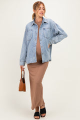 woman wearing a brown maternity maxi dress and a light blue oversized denim jacket, holding a brown handbag and showing her baby bump