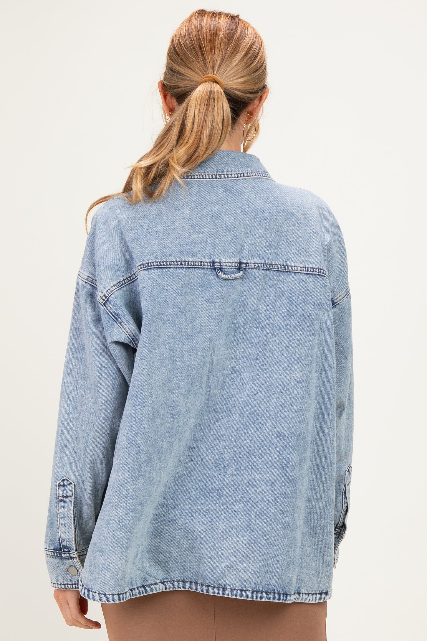 woman wearing a light blue oversized denim jacket, styled with a casual look, showing the back view