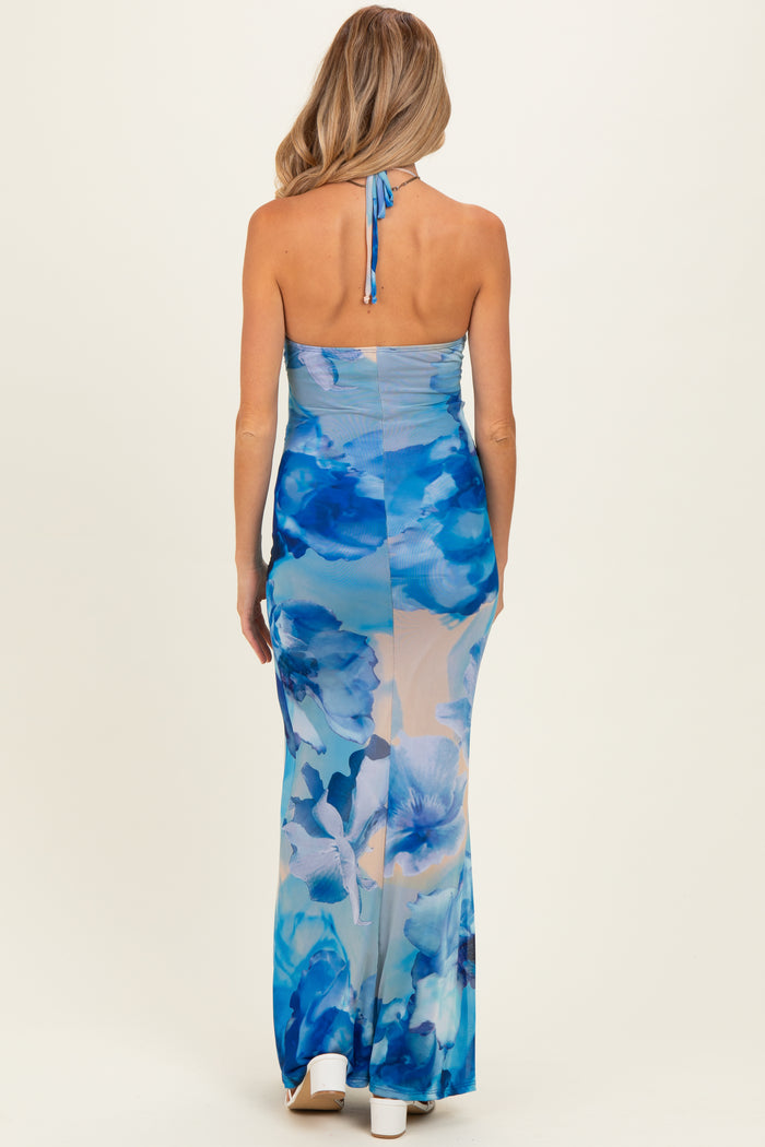 woman wearing a blue floral maternity dress with a halter neck and a long, flowing skirt, showcasing a baby bump