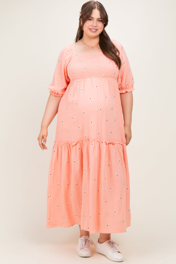 woman wearing a coral pink maternity plus maxi dress with puff sleeves and embroidered details, featuring a baby bump