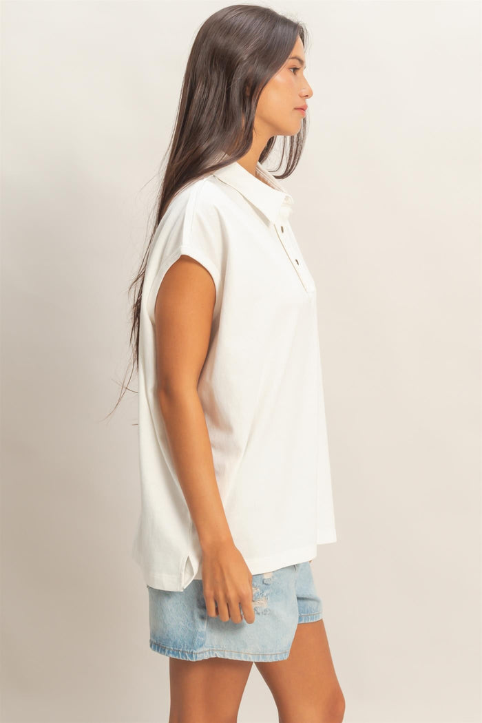 woman wearing a white short sleeve polo shirt and denim shorts, standing sideways with long hair down