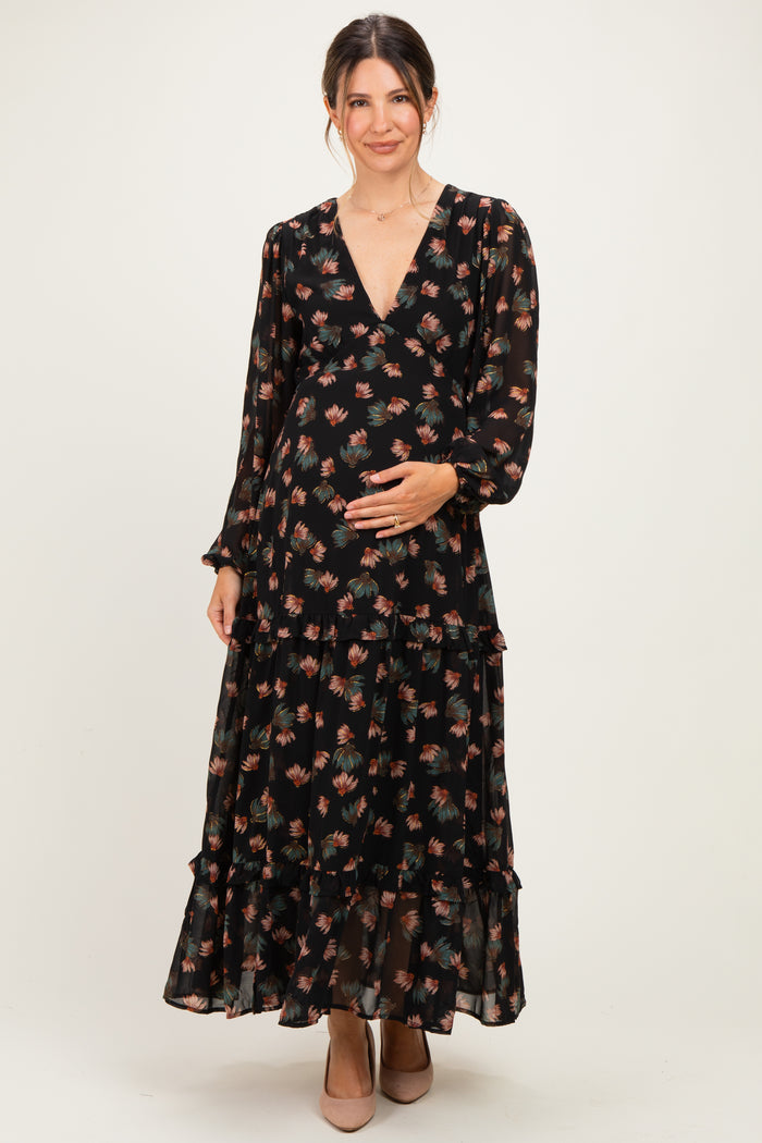 woman wearing a black floral maternity maxi dress with long sleeves and a tiered skirt, holding her baby bump