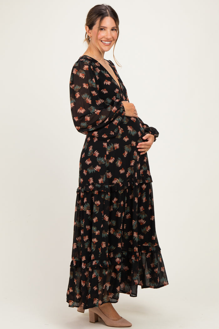 woman wearing a black floral maternity maxi dress with long sleeves and a ruffled hem, cradling her baby bump