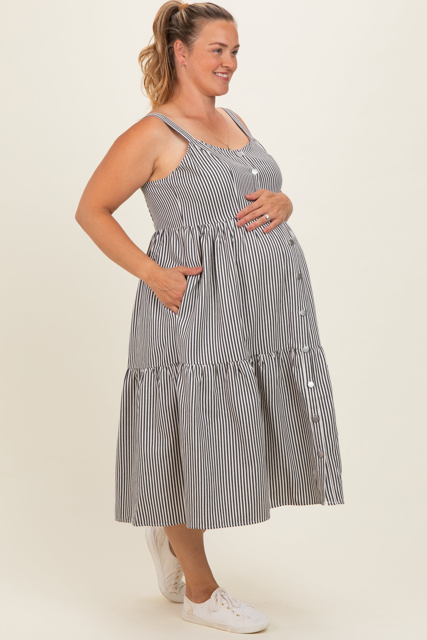 woman wearing a black and white striped maternity dress with pockets and buttons, showing her baby bump