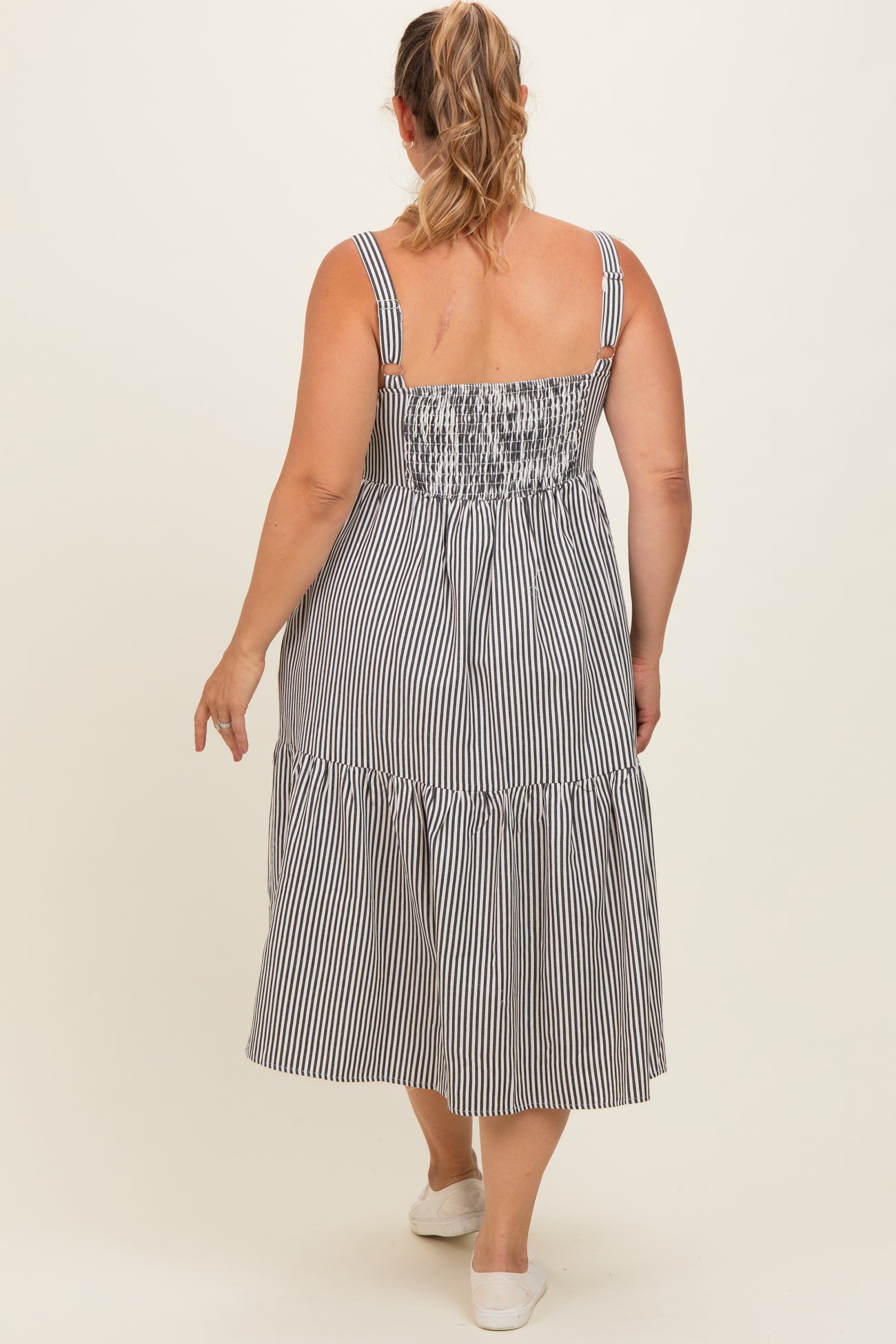 woman wearing a striped maternity plus dress with a smocked bodice and tiered skirt, showing the back view