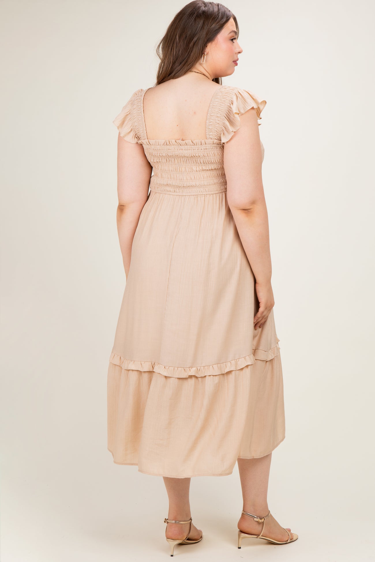 woman wearing a blush pink maternity plus dress with ruffled sleeves and a tiered hem, showcasing a relaxed fit