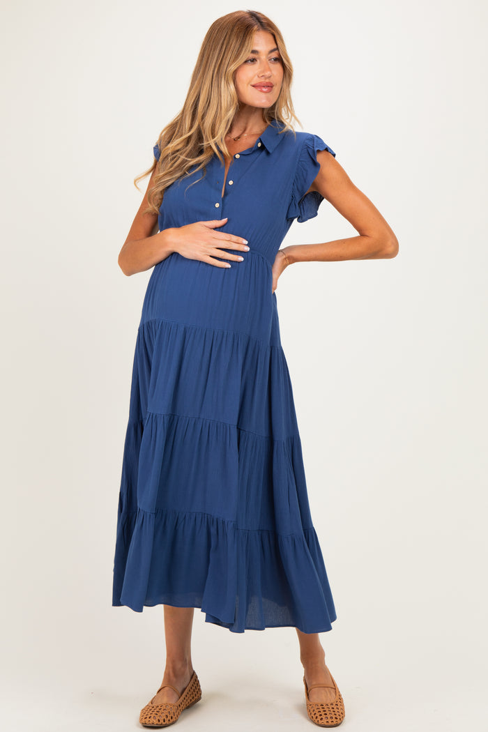 woman wearing a blue maternity dress with short sleeves and tiered ruffles, holding her baby bump