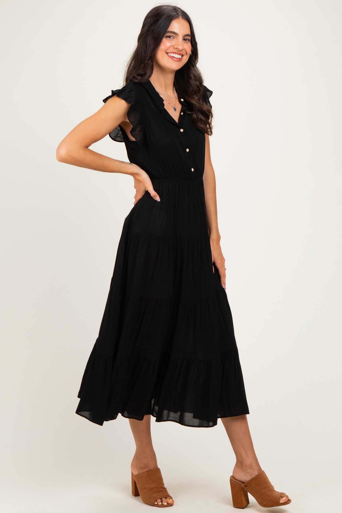woman wearing a black tiered midi dress with ruffle sleeves and buttons, styled with brown heeled sandals