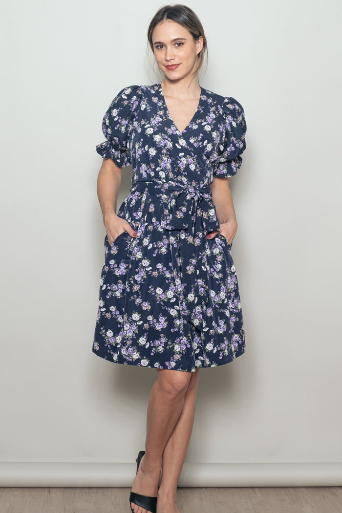 woman wearing a navy blue floral wrap dress with puff sleeves and pockets, accessorized with heels
