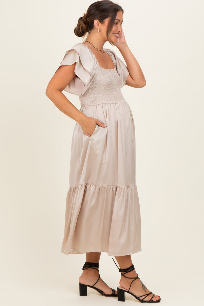 woman wearing a beige maternity dress with tiered skirt, puff sleeves, and side pockets, showing her baby bump