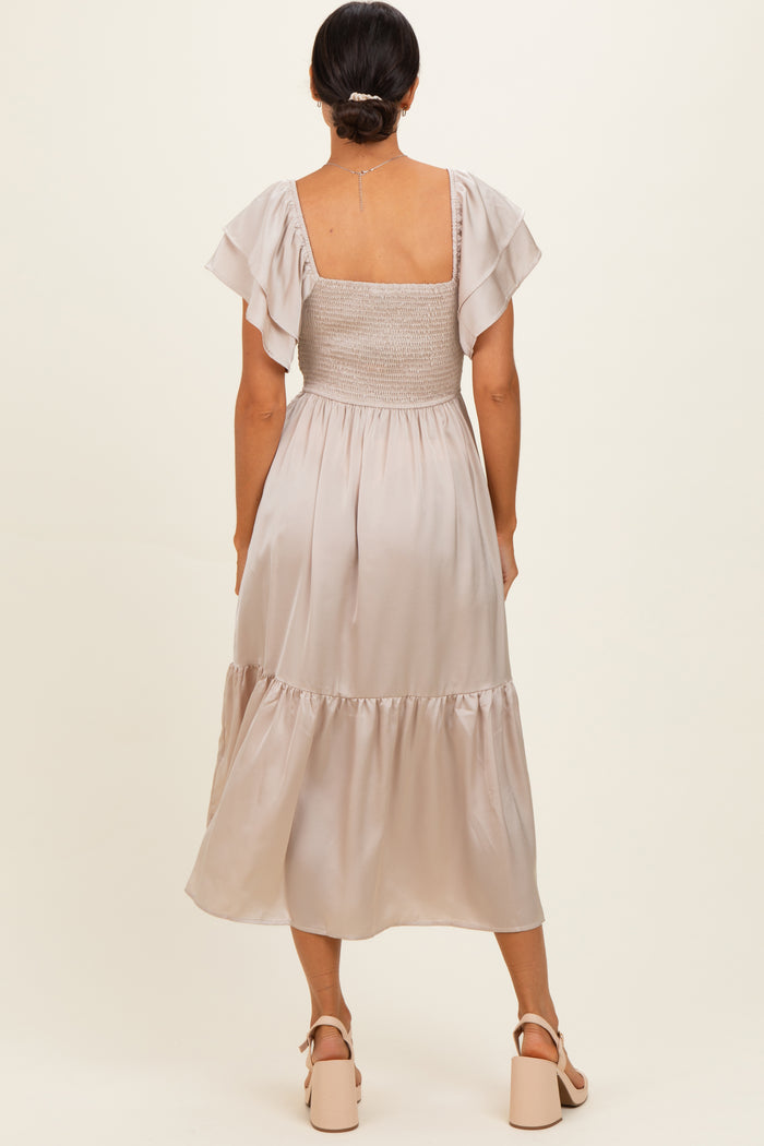 woman wearing a beige midi dress with a smocked bodice and flutter sleeves, viewed from the back