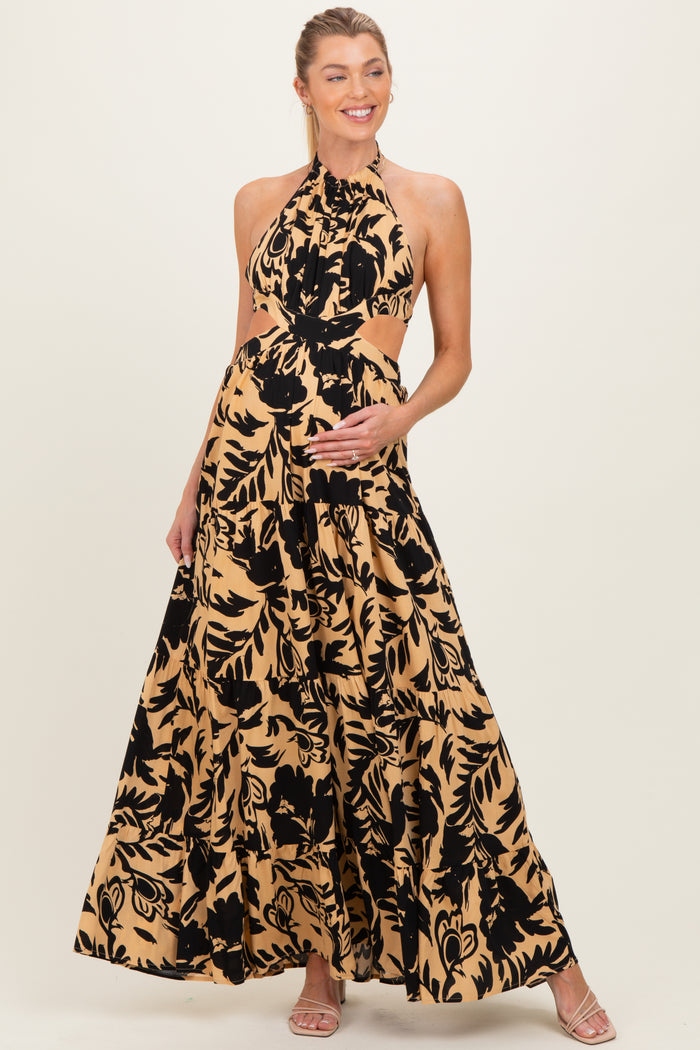 woman wearing a black and tan floral print maternity maxi dress, showing her baby bump with a halter neckline and cut-out details