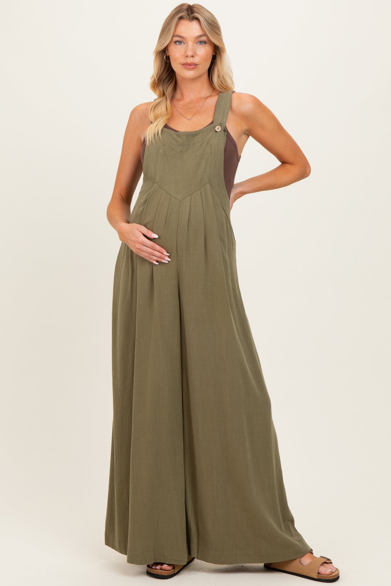 woman wearing a green maternity jumpsuit with adjustable straps and a baby bump visible