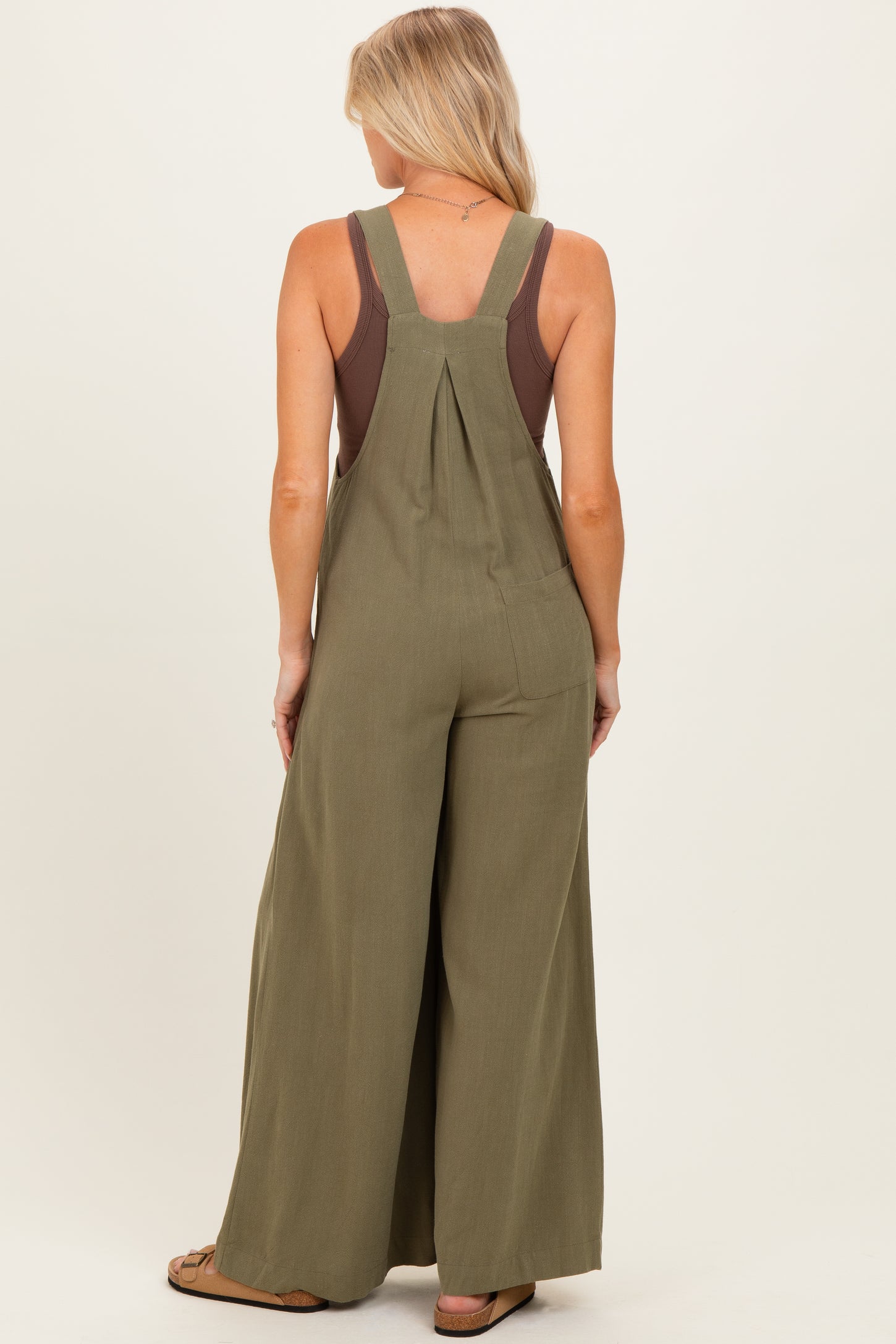 woman wearing an olive green maternity jumpsuit with wide legs and a relaxed fit, showcasing adjustable straps