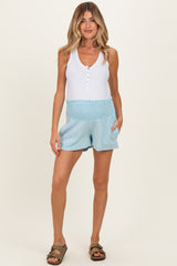 woman wearing a white tank top and light blue maternity shorts with a smocked waistband and pockets