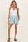 woman wearing a white tank top and light blue maternity shorts with a smocked waistband and pockets