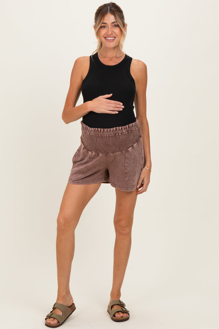 woman wearing a black tank top and brown maternity shorts, holding her baby bump