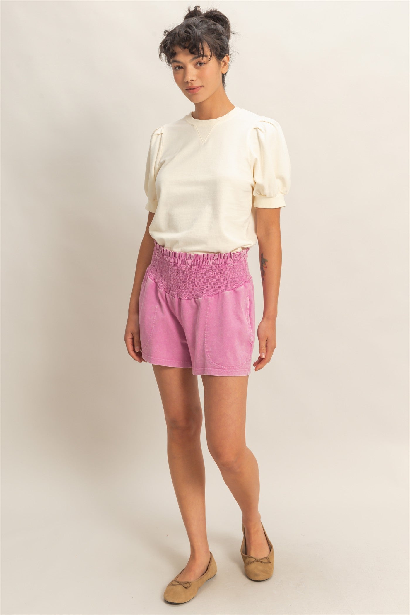 woman wearing a cream puff sleeve top and pink shorts with an elastic waistband