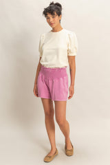 woman wearing a cream puff sleeve top and pink shorts with an elastic waistband