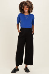 woman wearing a bright blue short sleeve top and black wide-leg maternity trousers with pockets