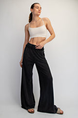 woman wearing a white cropped tank top and black wide-leg pants, posing with one hand on her hip