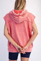 woman wearing a pink sleeveless hoodie with a hood, seen from the back, hands clasped behind her back