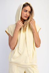 woman wearing a light yellow sleeveless hoodie with a front pocket and long tie details around the neckline