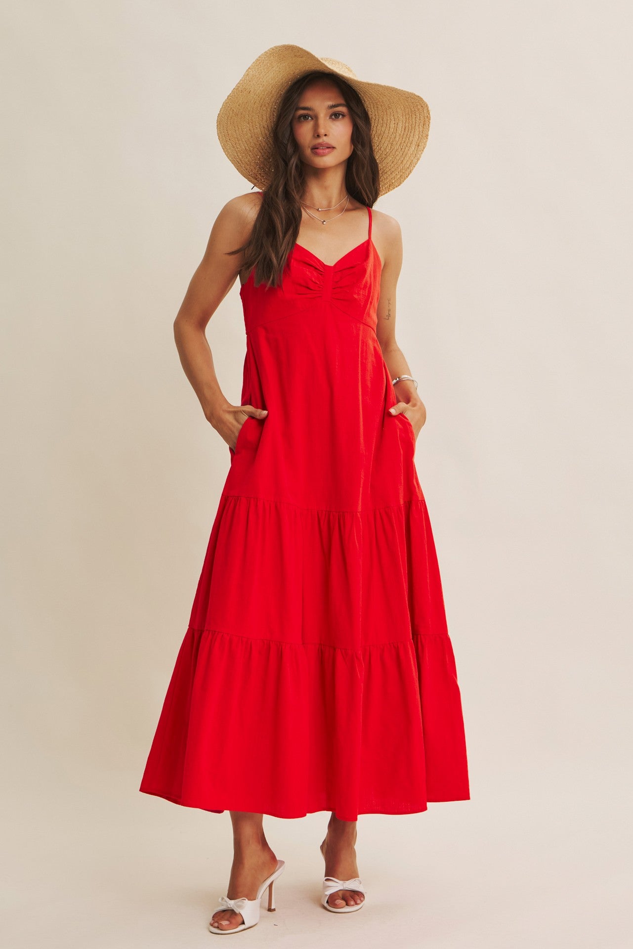 woman wearing a red tiered maxi dress with a sweetheart neckline and pockets, styled with a wide-brimmed straw hat