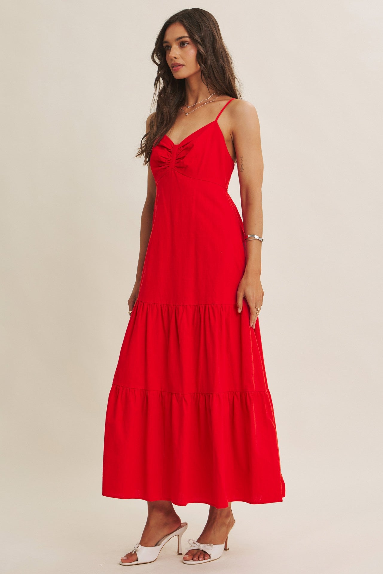 woman wearing a bright red maxi dress with tie detail and tiered skirt, standing against a neutral background