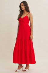 woman wearing a bright red maxi dress with tie detail and tiered skirt, standing against a neutral background