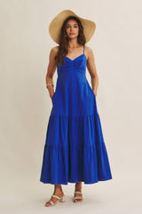 woman wearing a vibrant blue maxi dress with a tiered skirt and spaghetti straps, styled with a straw hat and sandals