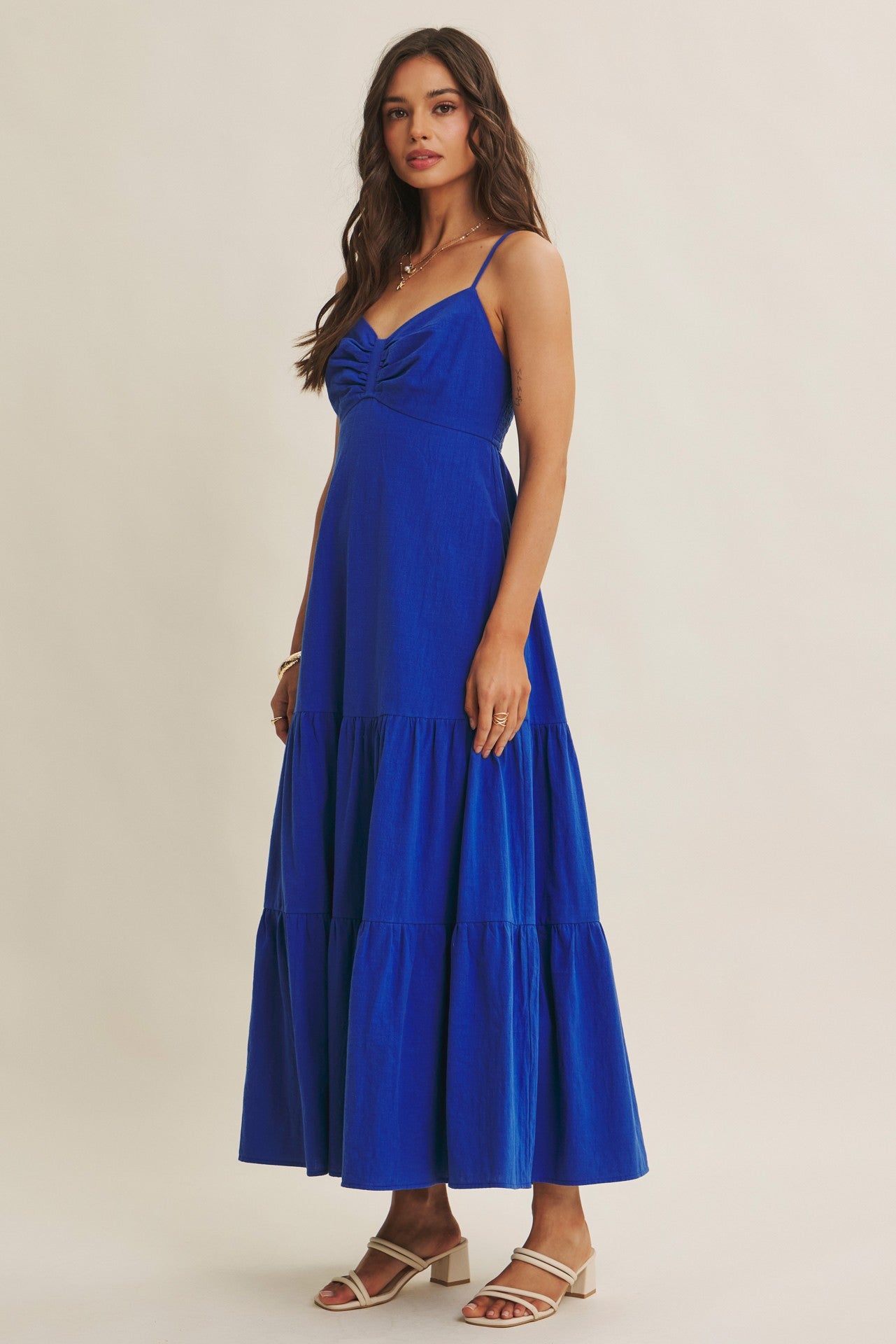 woman wearing a blue sleeveless maxi dress with a ruched bodice and tiered skirt, standing on a neutral background