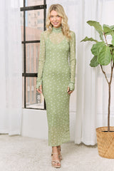 woman wearing a sheer green long sleeve dress with white polka dots and a high neck standing by a window