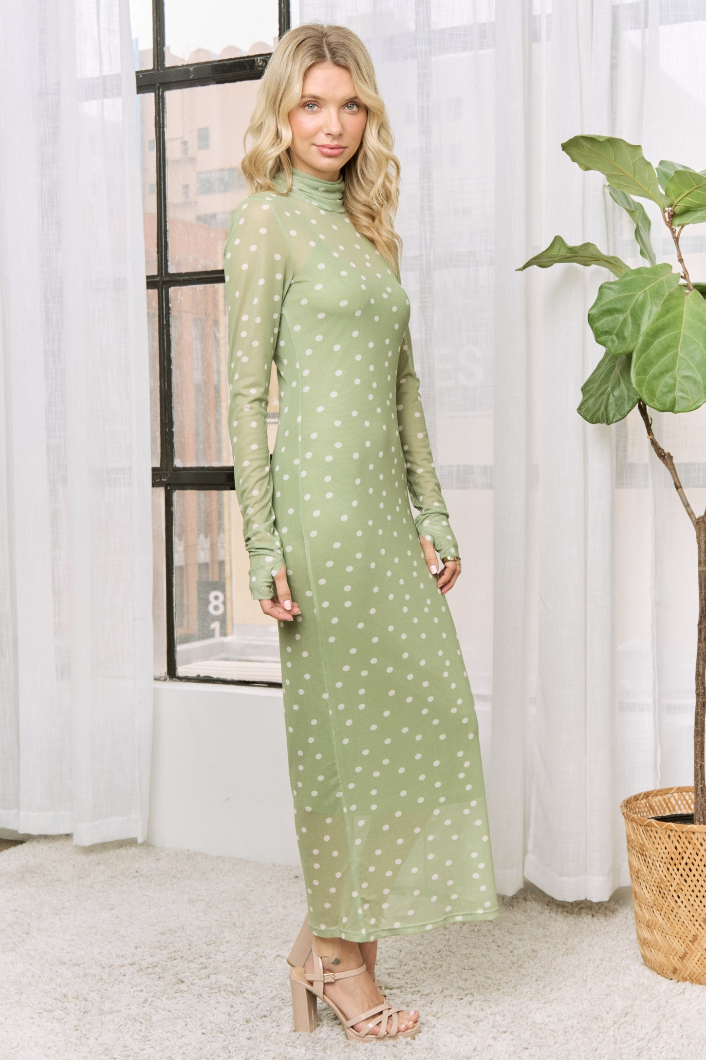 woman wearing a long sleeve light green polka dot maxi dress and posing next to a window