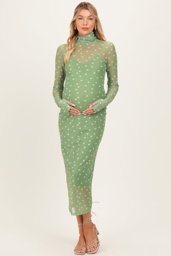 woman wearing a green sheer maternity dress with white polka dots and long sleeves, gently cradling her baby bump