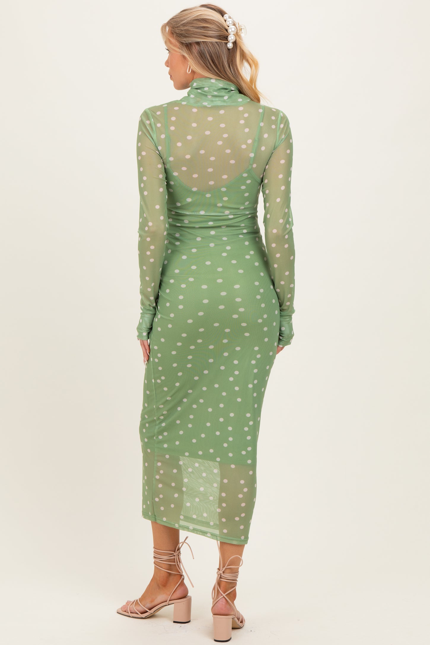 woman wearing a sheer green maternity dress with white polka dots, showing her baby bump from the back