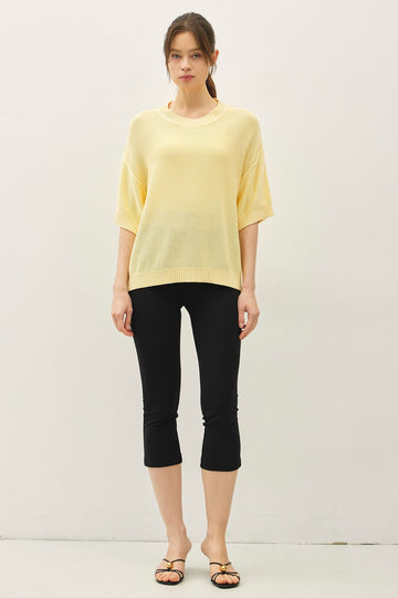 woman wearing a light yellow oversized sweater and black capri leggings, standing against a neutral background