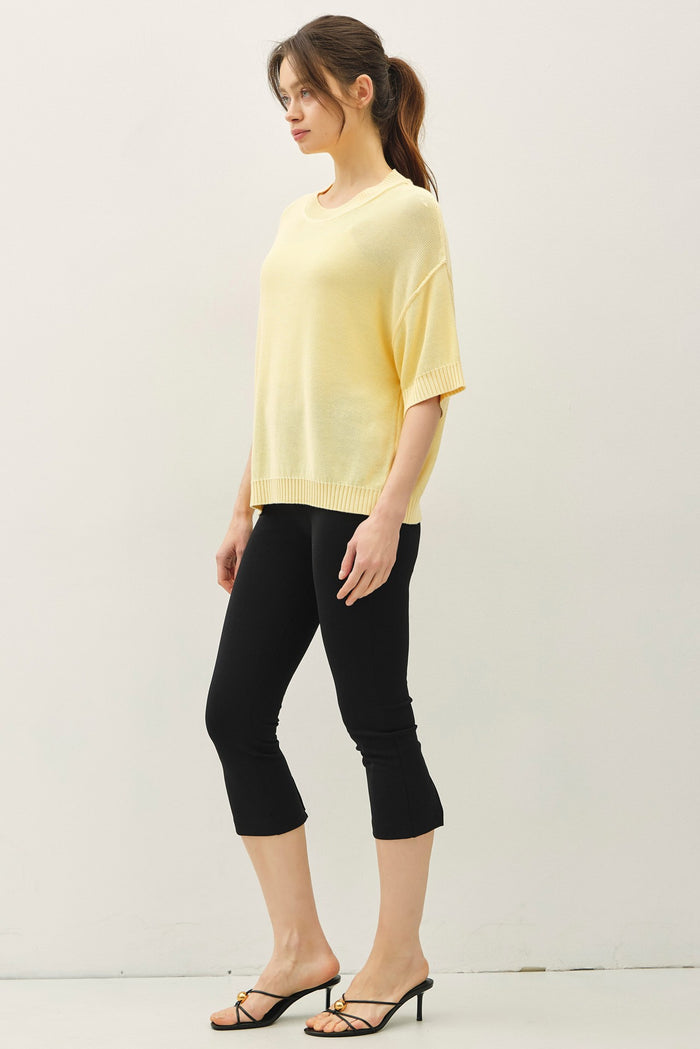 woman wearing a loose-fitting yellow knit top and black cropped leggings with strappy sandals