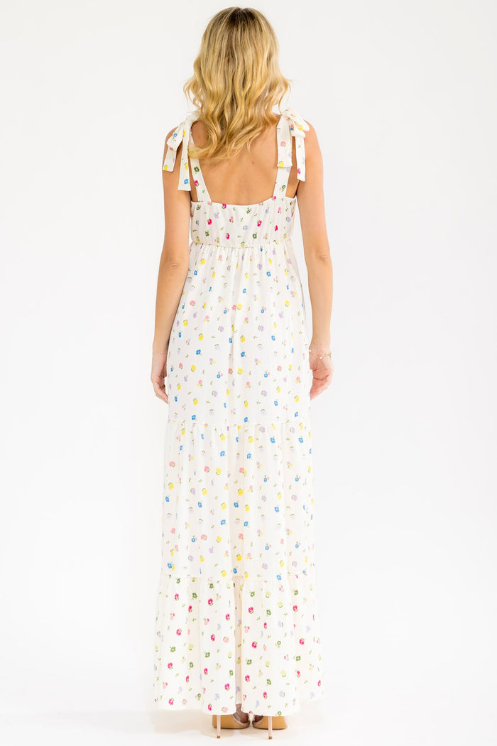 woman wearing a white floral maxi dress with adjustable tie straps and a tiered skirt, shown from the back