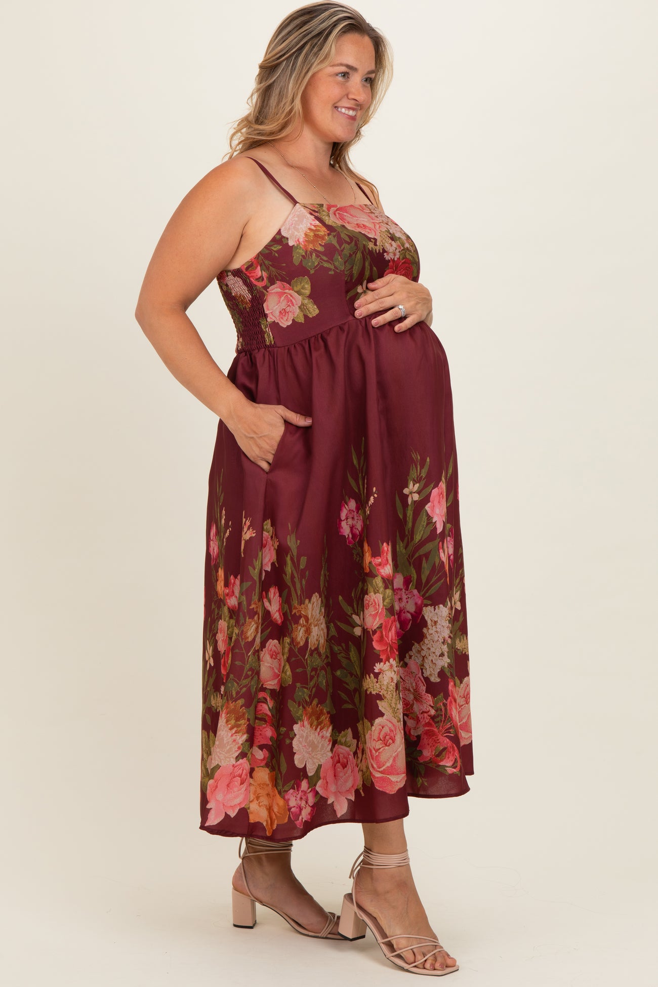 woman wearing a burgundy floral maternity dress with pockets, fitted bodice, and flowing skirt, holding her baby bump