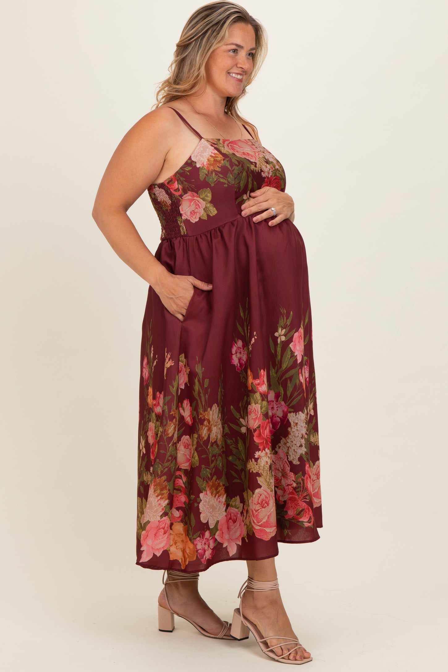 woman wearing a burgundy floral maternity dress with pockets, fitted bodice, and flowing skirt, holding her baby bump
