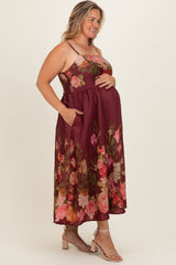 woman wearing a burgundy floral maternity dress with pockets, fitted bodice, and flowing skirt, holding her baby bump