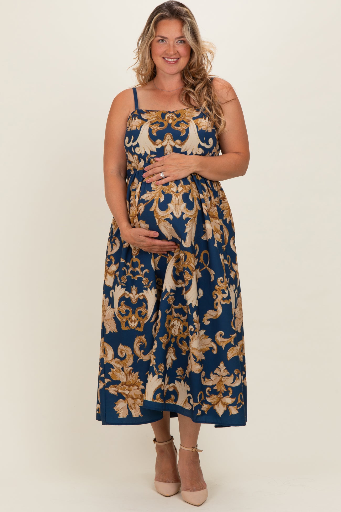 woman wearing a navy blue floral print maternity dress with spaghetti straps and holding her baby bump