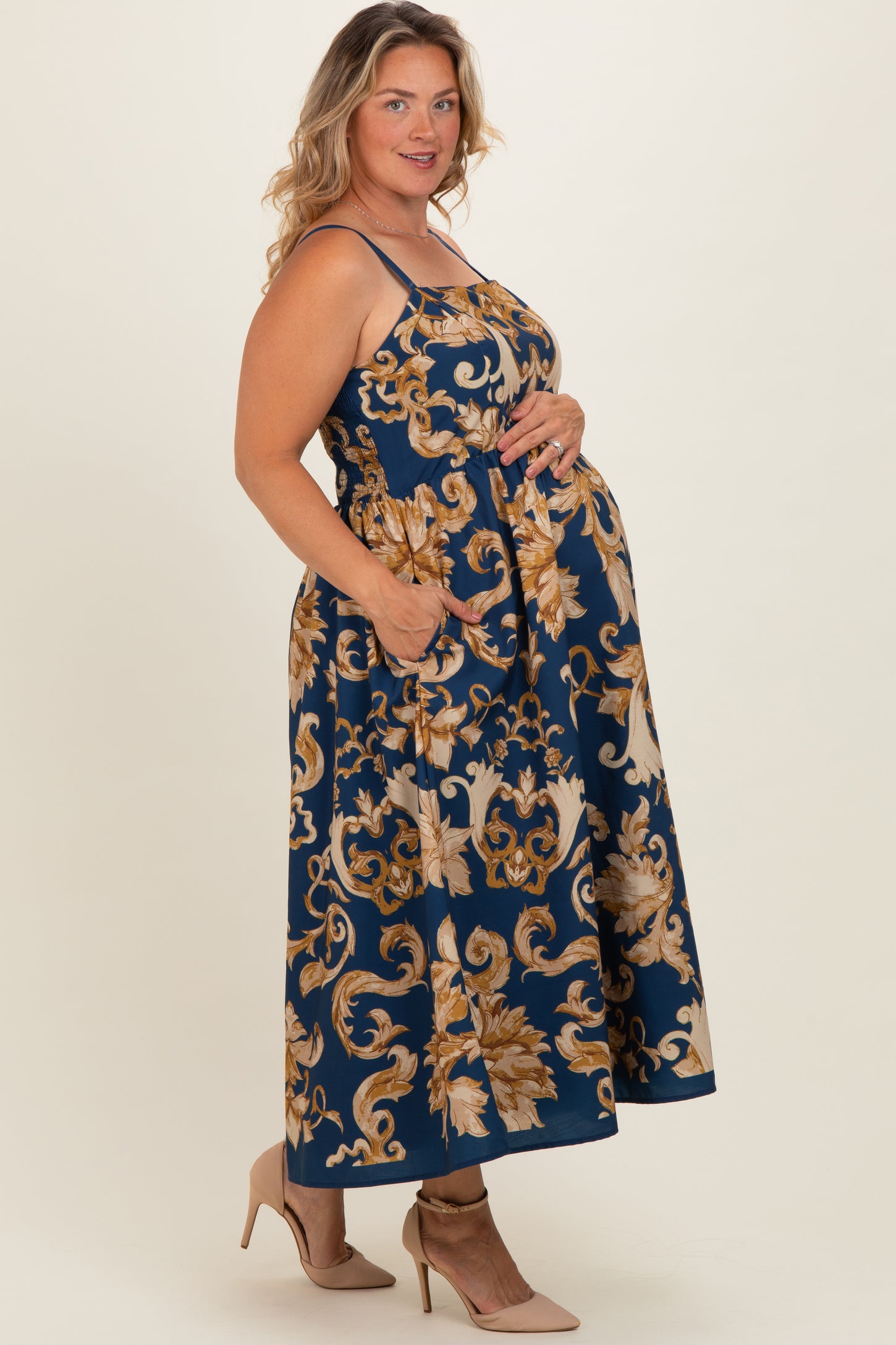 woman wearing a navy blue floral maternity maxi dress with adjustable straps and pockets, showcasing her baby bump