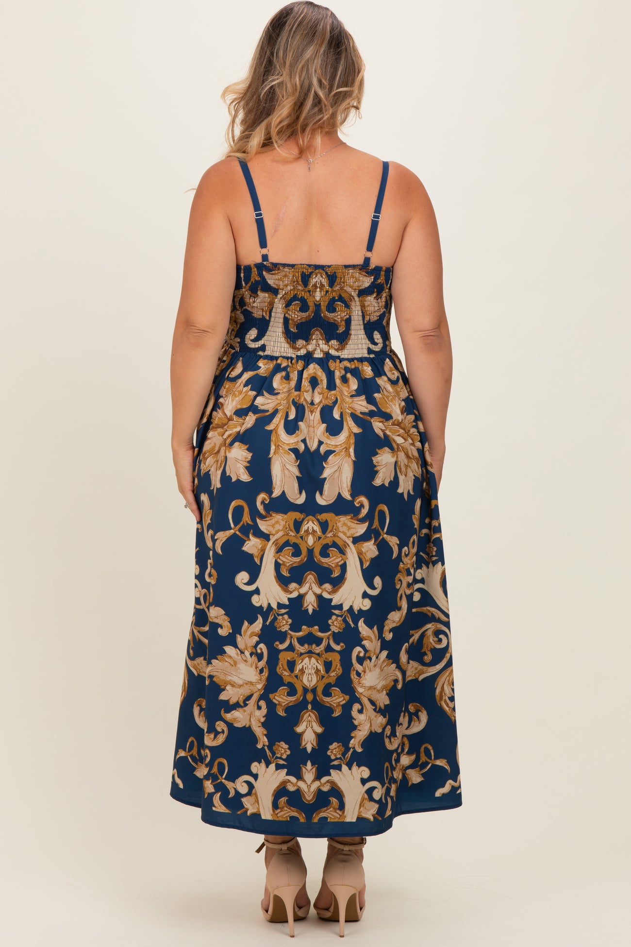 woman wearing a navy blue maternity plus maxi dress with a floral pattern and adjustable straps, viewed from the back