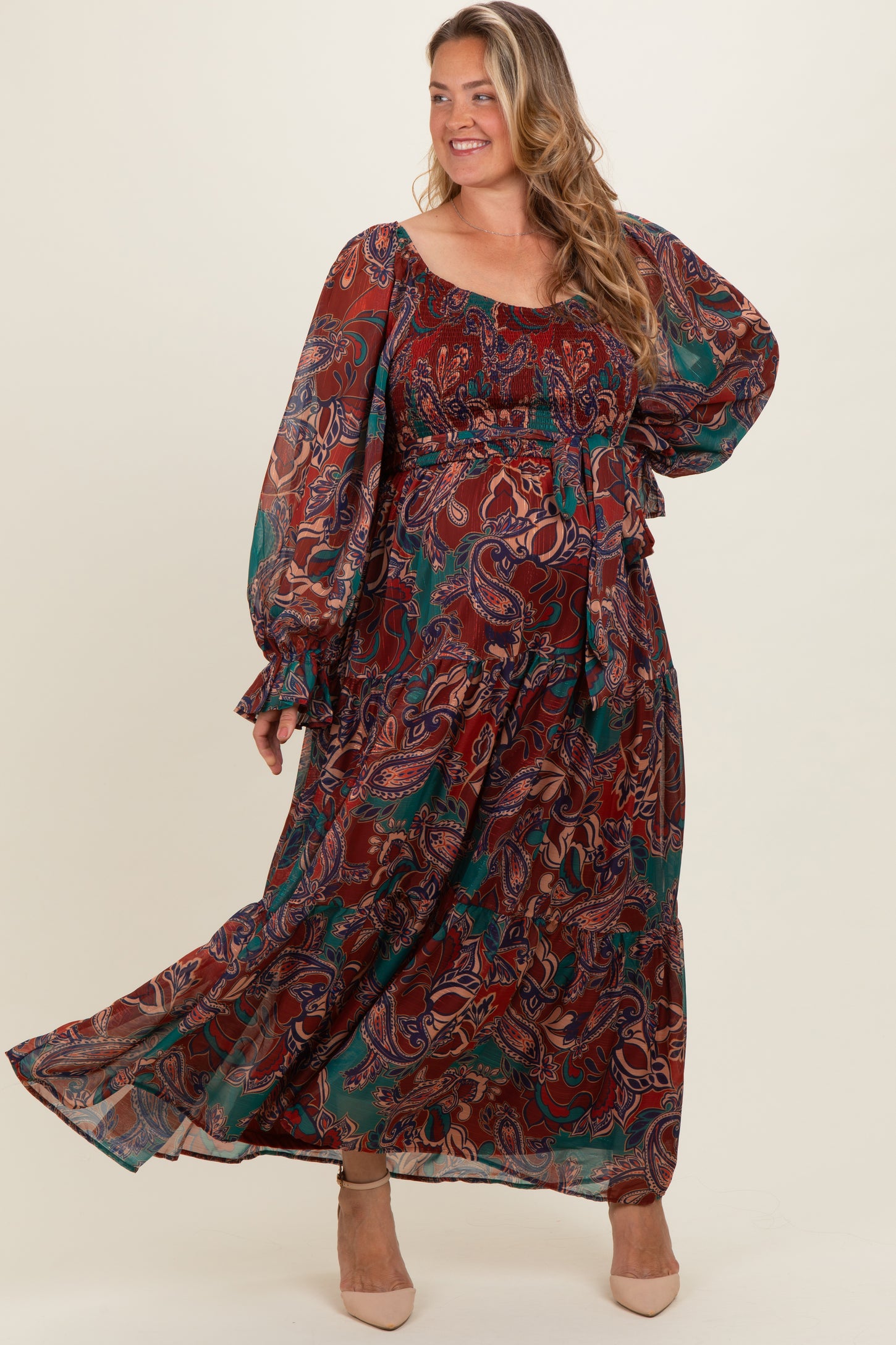 woman wearing a multi-colored paisley print maternity plus maxi dress with long sleeves and a cinched waist, showing a baby bump